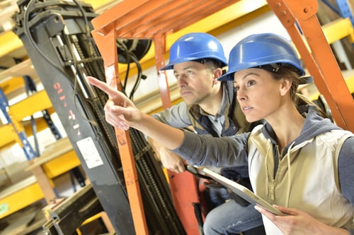 Two warehouse operators checking stock levels on a forklift in a multi-site retail warehouse
